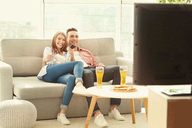 casal alegre sentado no sofá a ver televisão