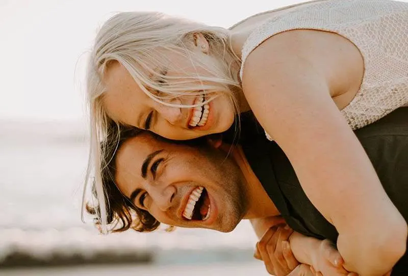 close up photo of smiling man piggybacking happy blonde woman outside