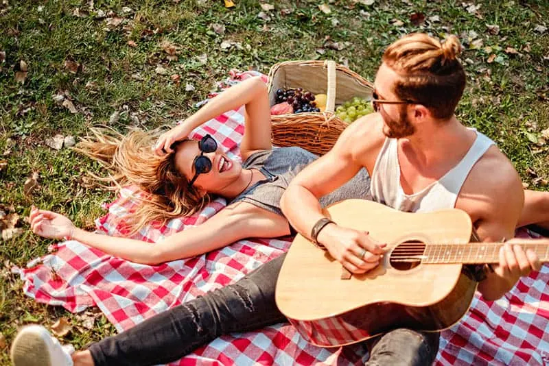 man playing guitar to smiling woman during picnic time