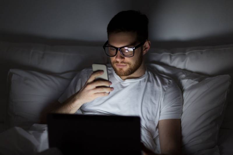 man wearing eyeglasses typing on his phone before sleep