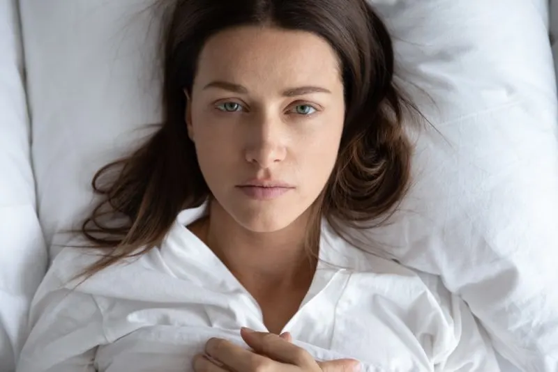 pensive and beautiful young woman lying in bed