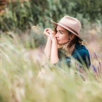 Sad woman with a hat looking into distance. Sitting in the grass.