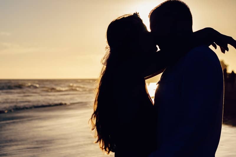 silhouette of couple kissing beside sea