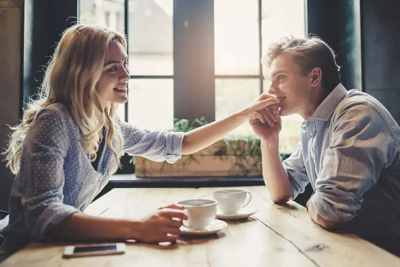 smiling man kisses woman hand at cafe