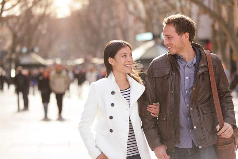 smiling woman holding a man and looking each other while walking on street