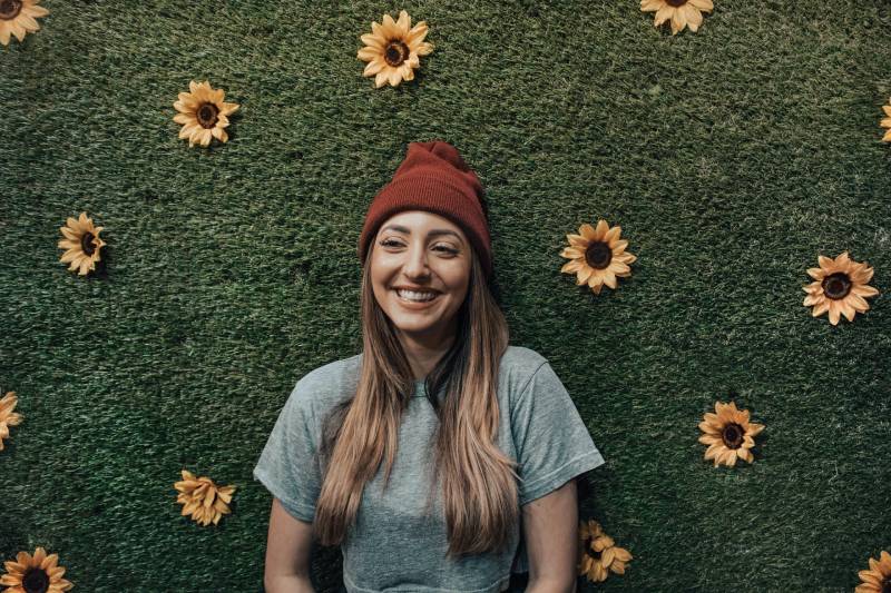 mujer sonriente apoyada en un muro de flores