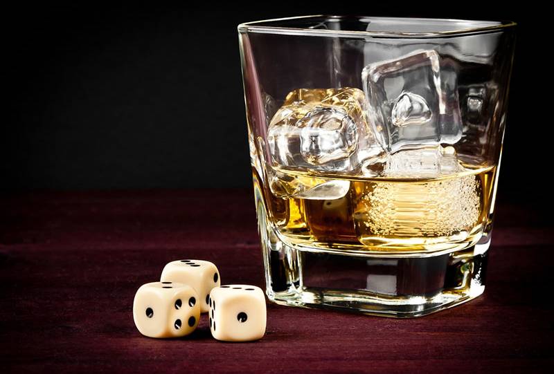 three dices next to glass with ice and whiskey