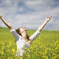 Mujer joven de pie en un campo de colza levantando los brazos