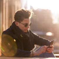 a handsome young man is sitting outside and using a smartphone