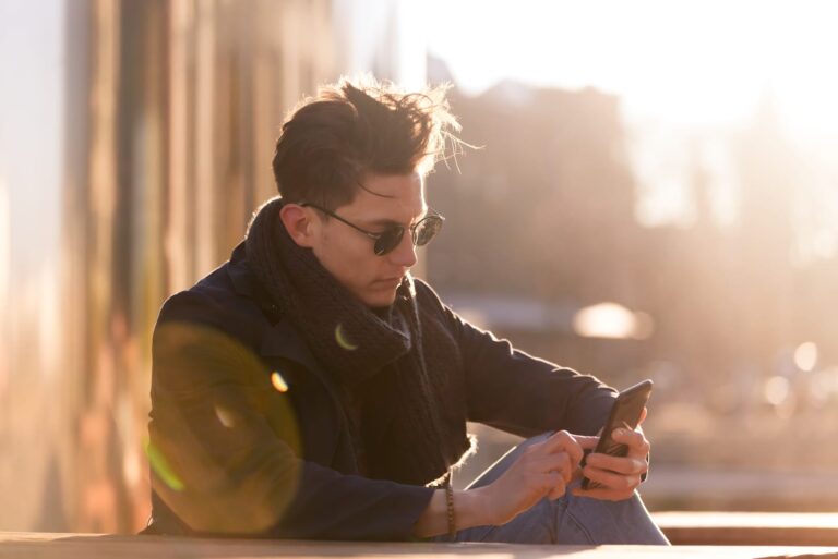 a handsome young man is sitting outside and using a smartphone
