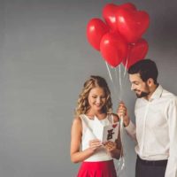 man holding red balloon while woman reading card