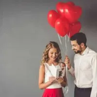 man holding red balloon while woman reading card
