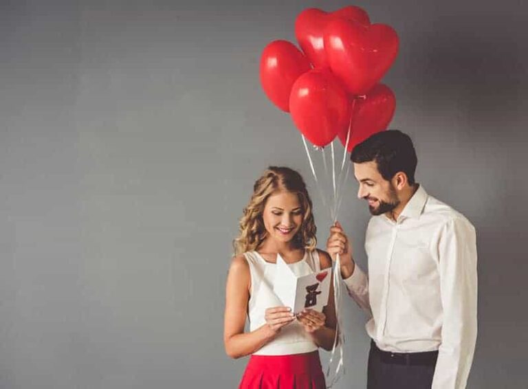 hombre sosteniendo globo rojo mientras mujer leyendo tarjeta