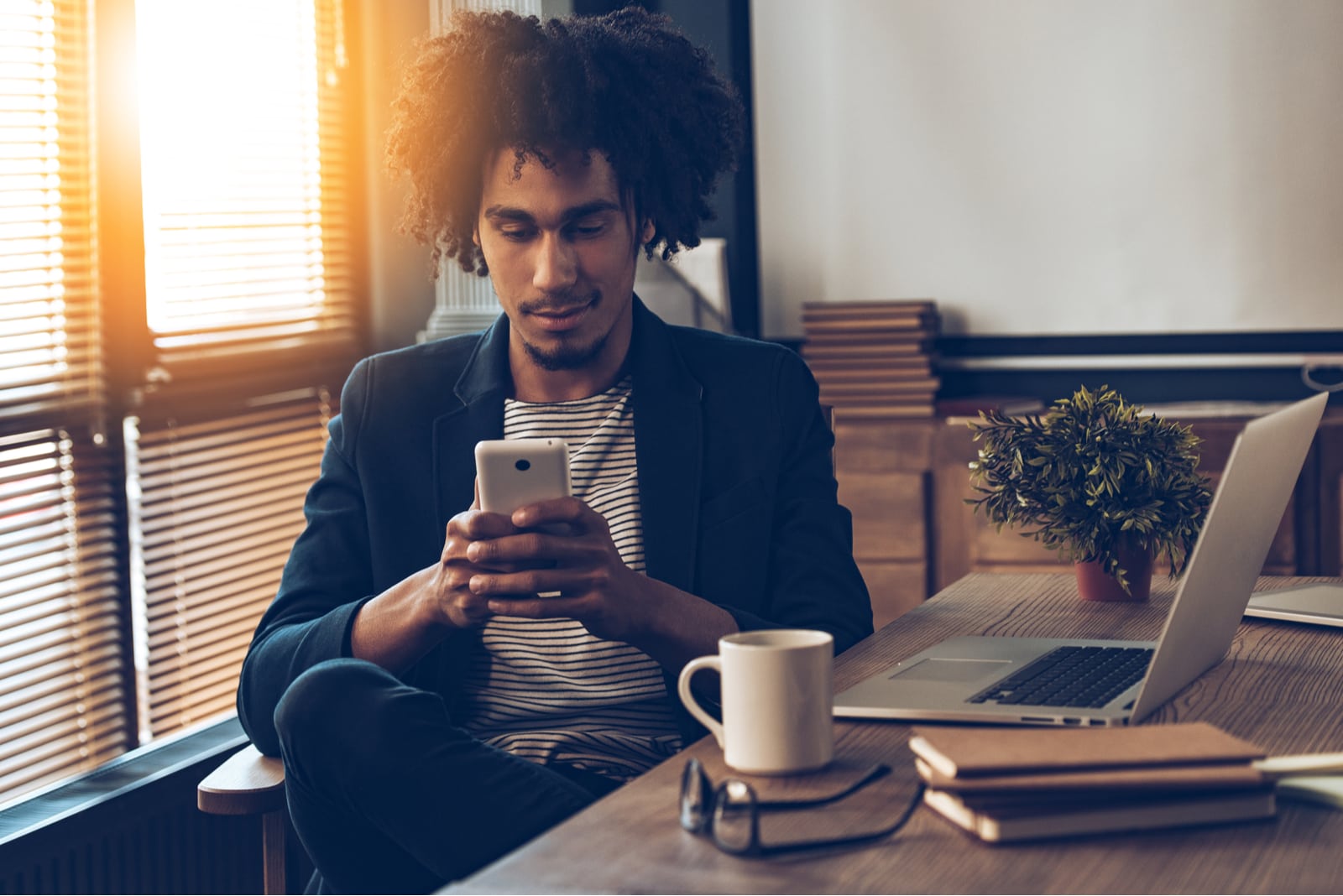 a handsome african american is sitting in the office and using a smartphone