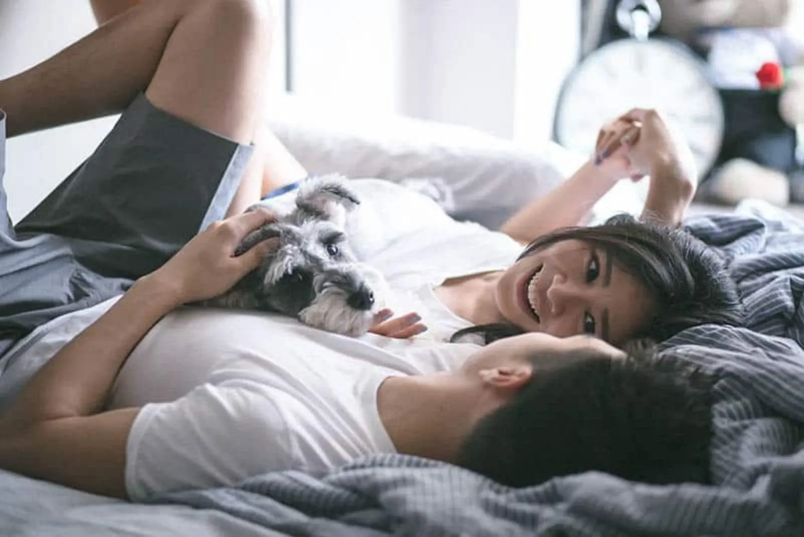 a man and a woman lie together on the bed embracing with a dog