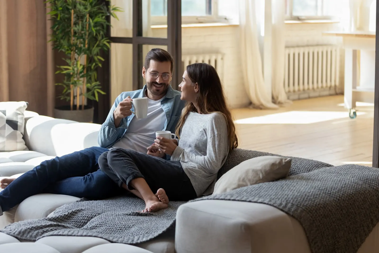 a man and a woman sit on the couch and drink coffee