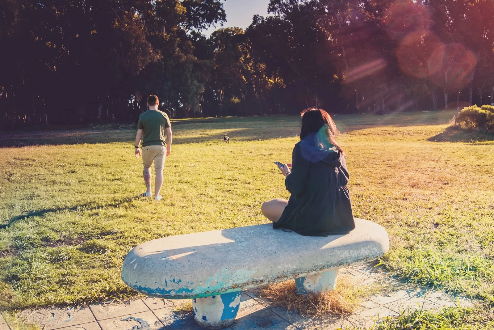 a man walks away from a woman sitting on a concrete bench in a park