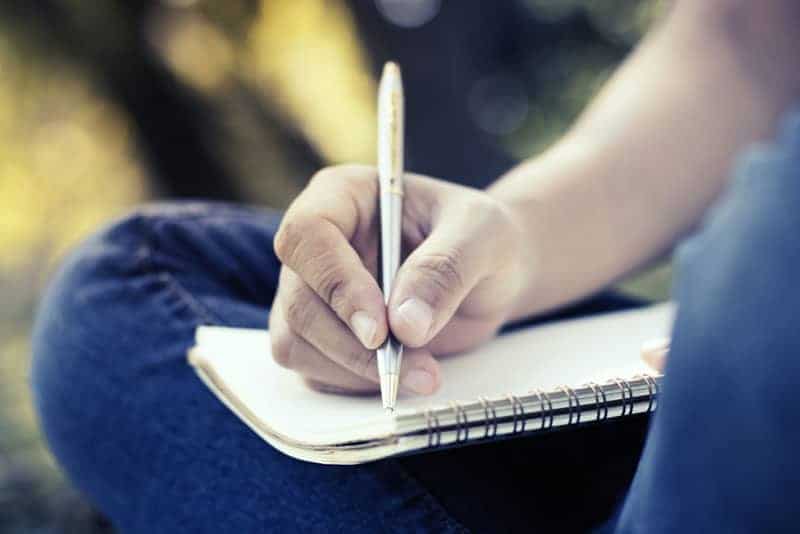 foto de cerca de un hombre que sostiene un bolígrafo y escribe en un cuaderno