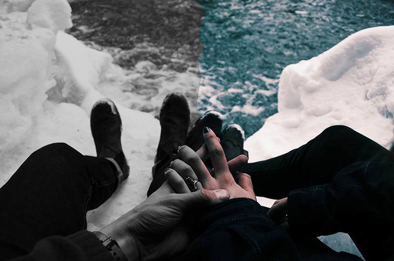 close up photo of man holds woman hands while sitting on snow rock