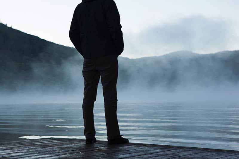 uomo in giacca nera e jeans neri in piedi davanti all'acqua