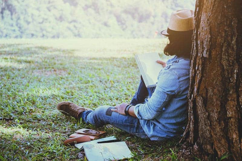 hombre apoyado en un árbol y leyendo un cuaderno