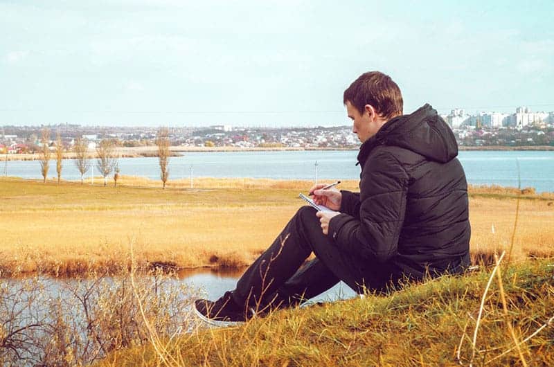 man writing on paper beside water