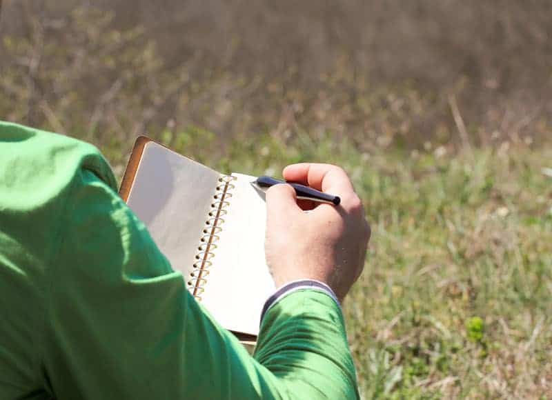 man writing on paper in field