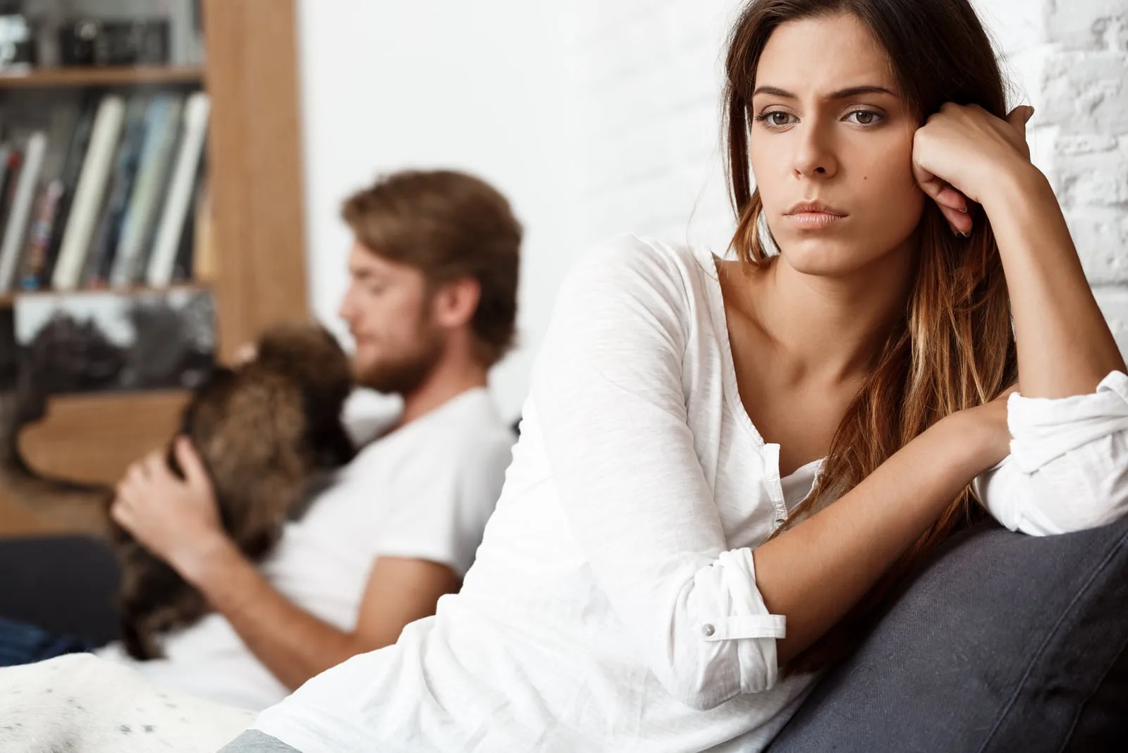 sad woman sitting apart from man who is playing with cat