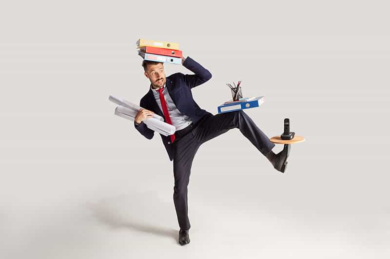 Young businessman in a suit juggling with office supplies in his office