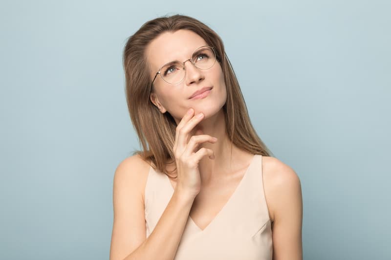 Millennial thoughtful woman in eyeglasses looking up