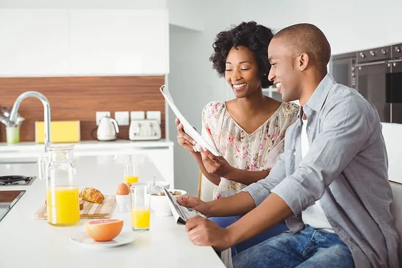 Smiling couple reading and eating breakfast together in the kitchen at home