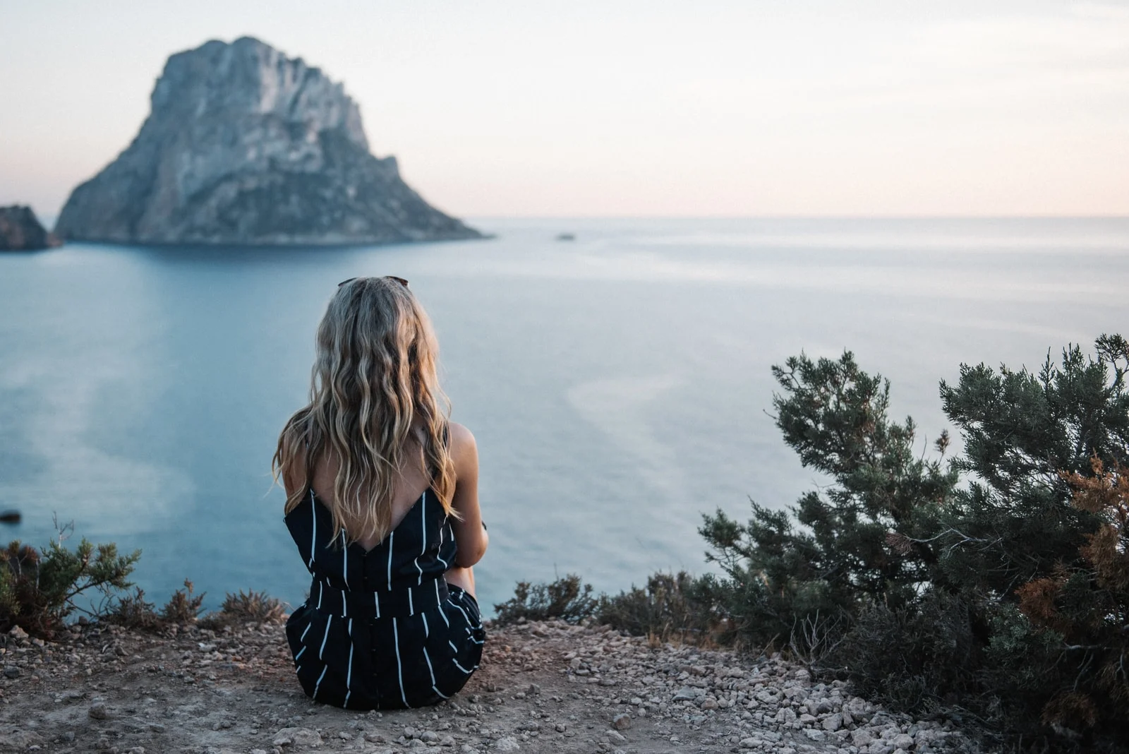 woman with long blond hair sitting by the sea alone