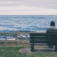 homem sentado sozinho em frente ao mar