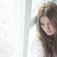 uma jovem triste sentada à janela