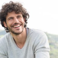 smiling curly haired man wearing shirt outside