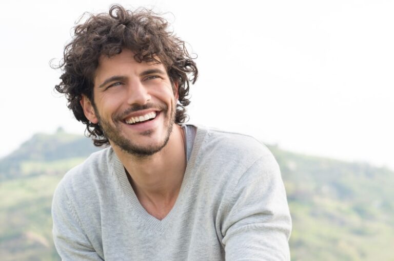 smiling curly haired man wearing shirt outside