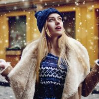 a beautiful blonde stands on the street and enjoys the falling snow