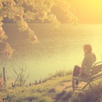 at sunset a woman sits alone on a bench by the river