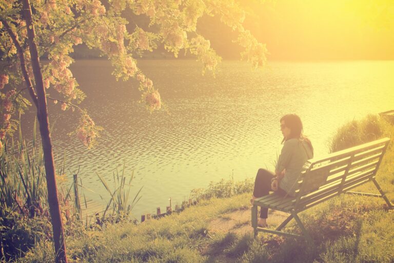 at sunset a woman sits alone on a bench by the river