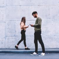 uomo e donna che camminano mentre scrivono sul loro smartphone