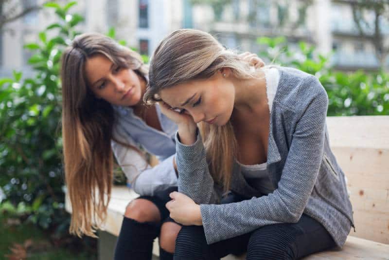 Mulher a confortar a sua amiga num banco de jardim