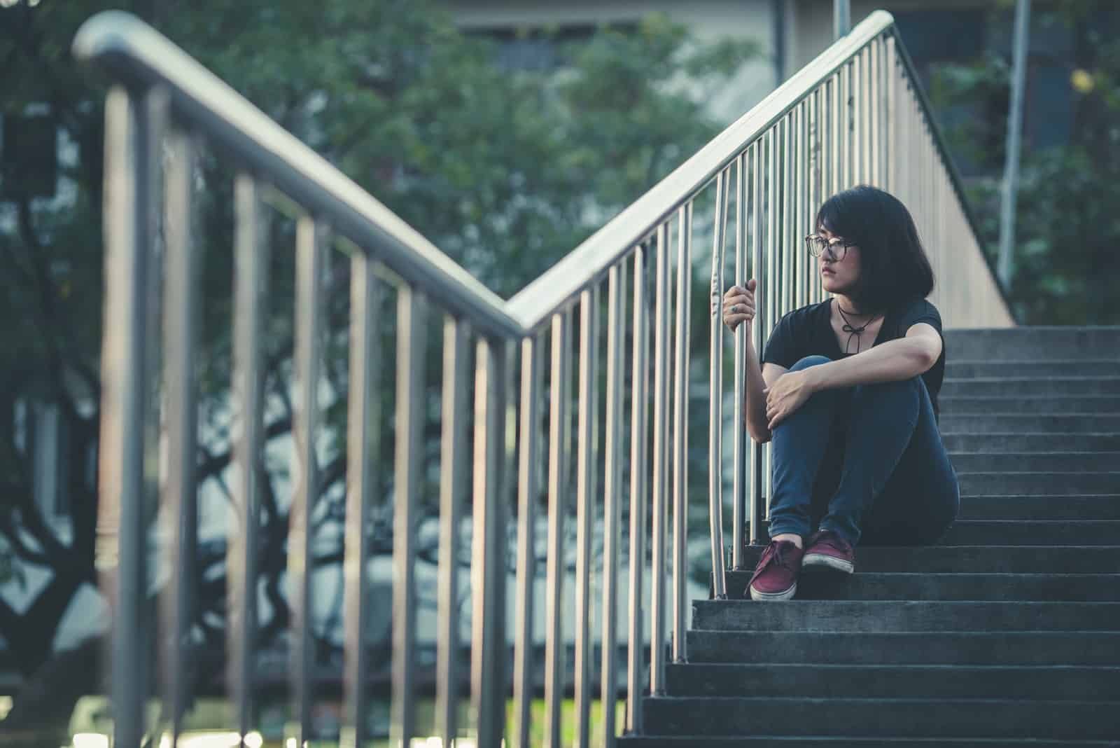 a sad girl with glasses is sitting outside on the stairs