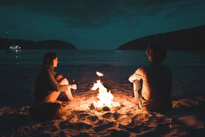 couple sitting by the fire on the beach
