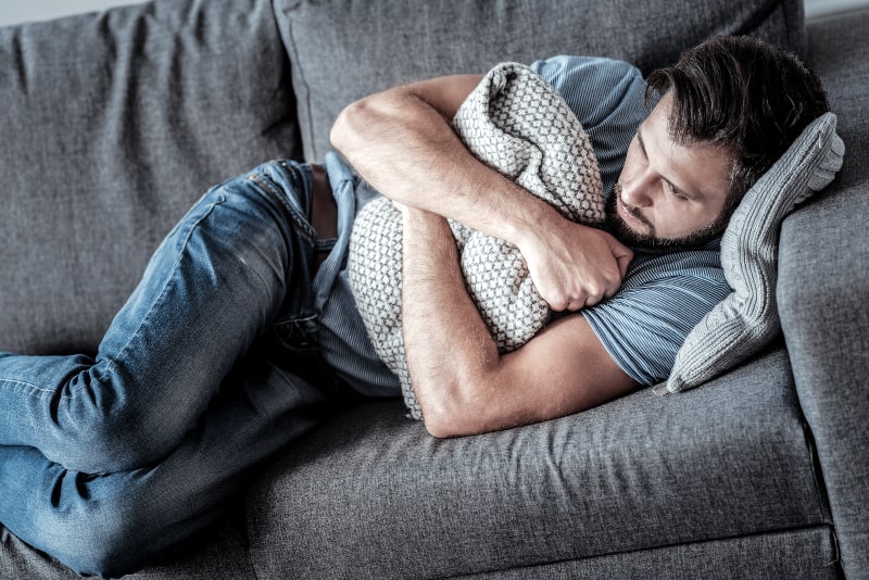 uomo depresso che abbraccia un cuscino mentre è sdraiato sul divano di casa