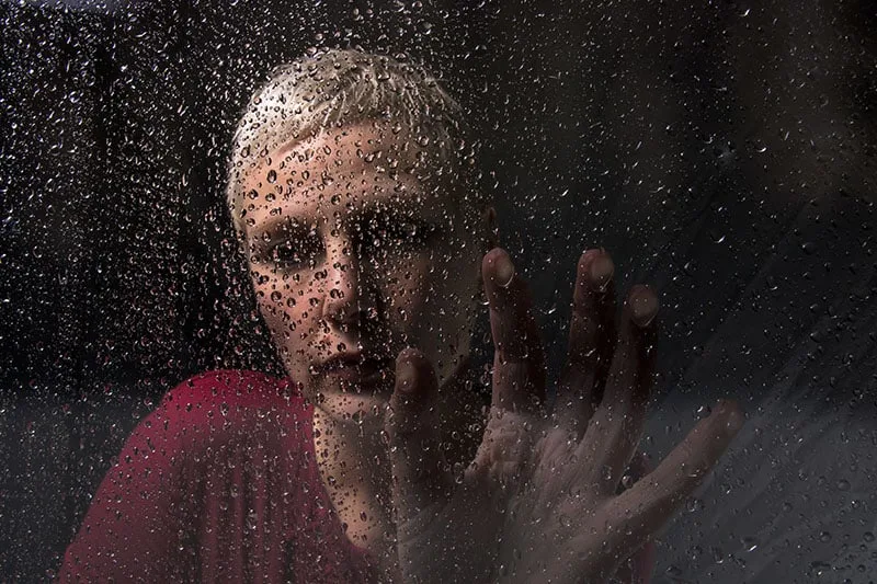 depressed woman sitting by the rainy glass
