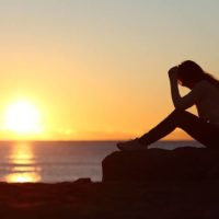 Silhouette di donna triste preoccupata sulla spiaggia al tramonto con il sole sullo sfondo