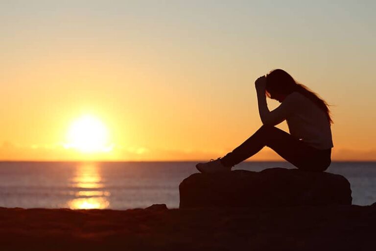 Silhouette di donna triste preoccupata sulla spiaggia al tramonto con il sole sullo sfondo