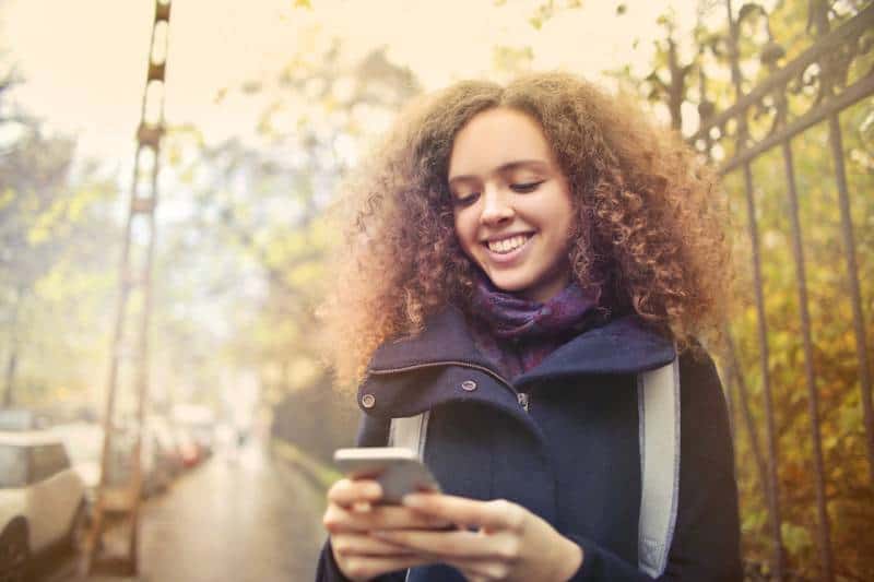 rapariga feliz a olhar para o telemóvel na rua