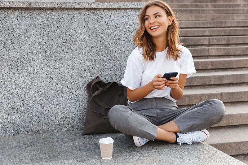 mujer feliz sentada al aire libre con smartphone