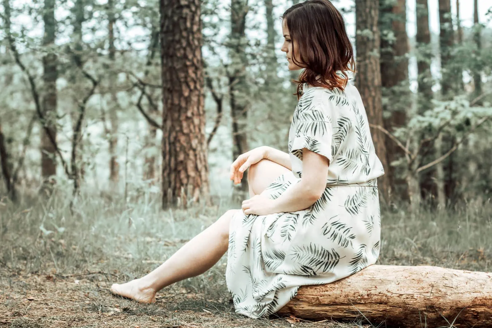 lonely woman in long white dress sitting in forest